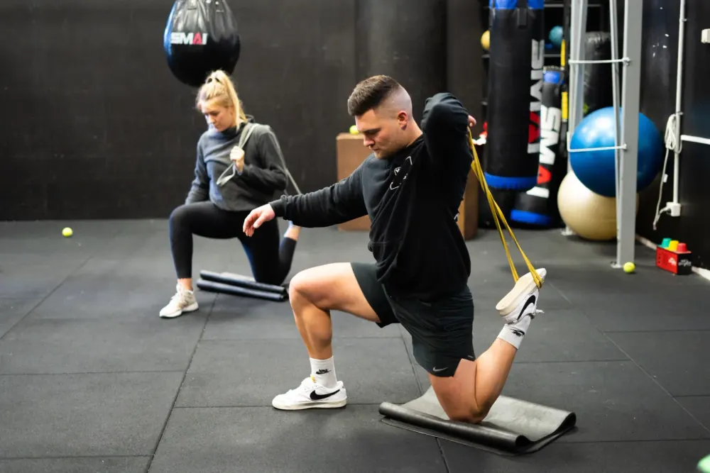 Two Compound members working through banded mobility and rehab exercises on the gym floor